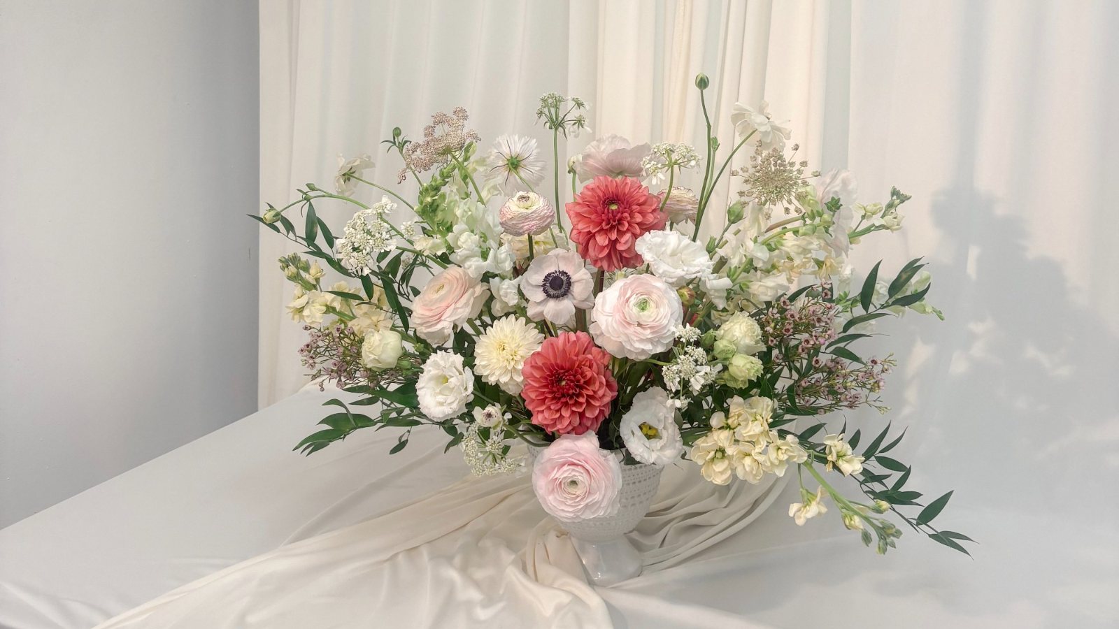 A garden-style arrangement of dahlias, anemones, ranunculus, and stock on a draped table