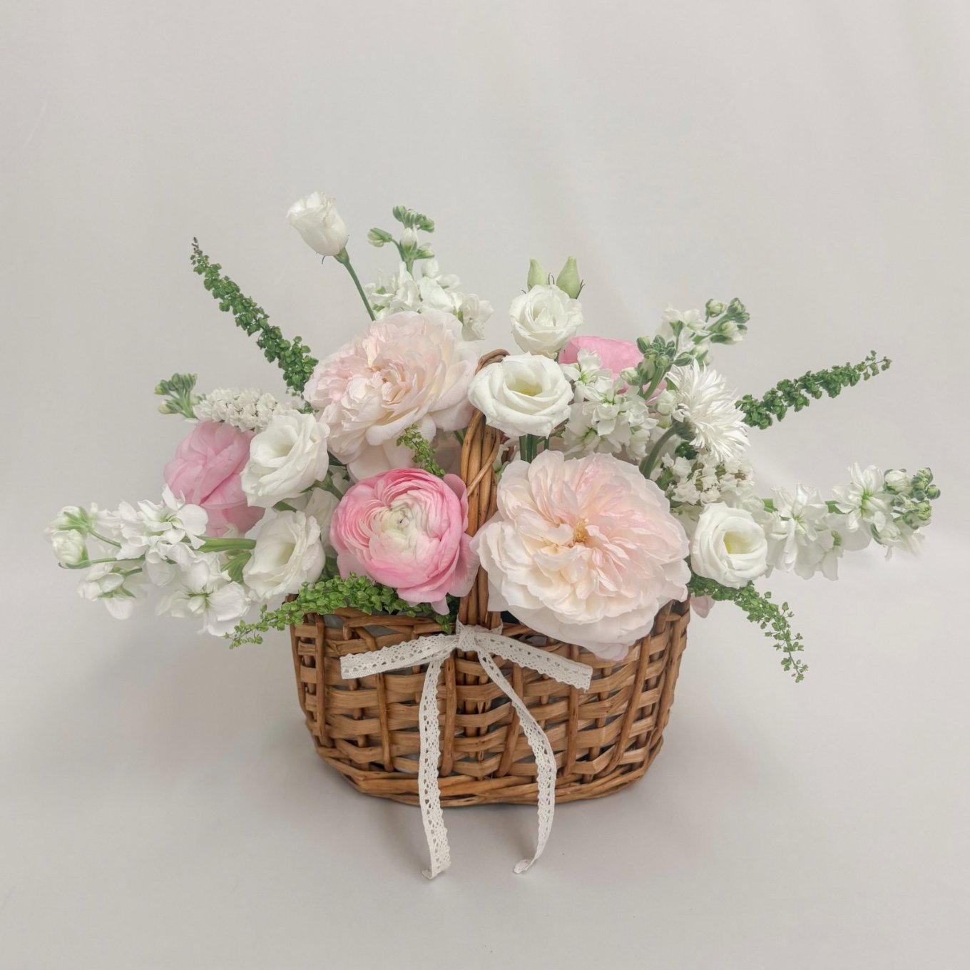 Signature Basket: blush garden roses, pink ranunculus, white lisianthus, and stock in a wicker basket tied with lace